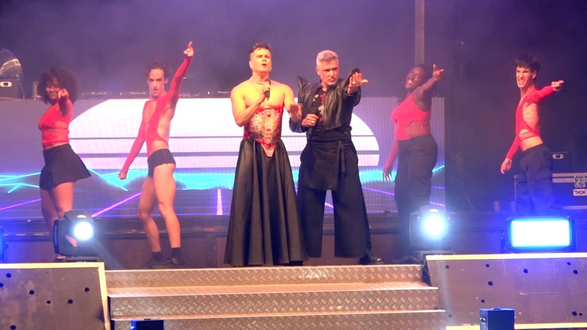 Eugin Vita con corsé rojo y Lui da Motta de cuero negro, los cuatro bailarines señalando al público bajo luz azul.